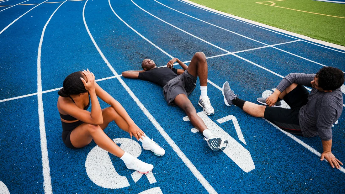 Varias personas descansando sentadas junto a una pista de atletismo azul después de entrenar